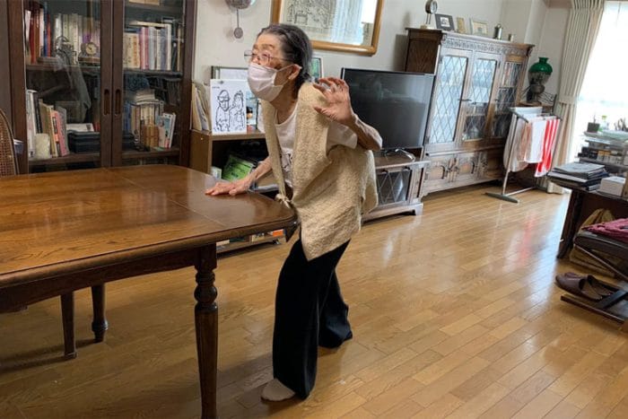 92-year-old Kimiko Hara performs a standing Front Step with one hand on a table for support